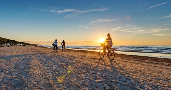 Cilvēki ar riteni brauc pa pludmales krastu
